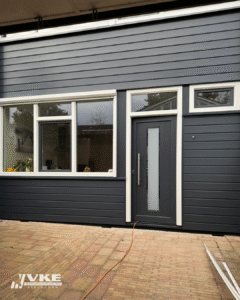 Donkergrijze kunststof voordeur met grote glasstrook en witte kozijnen, vakkundig geplaatst door VKE Apeldoorn bij een moderne woning.